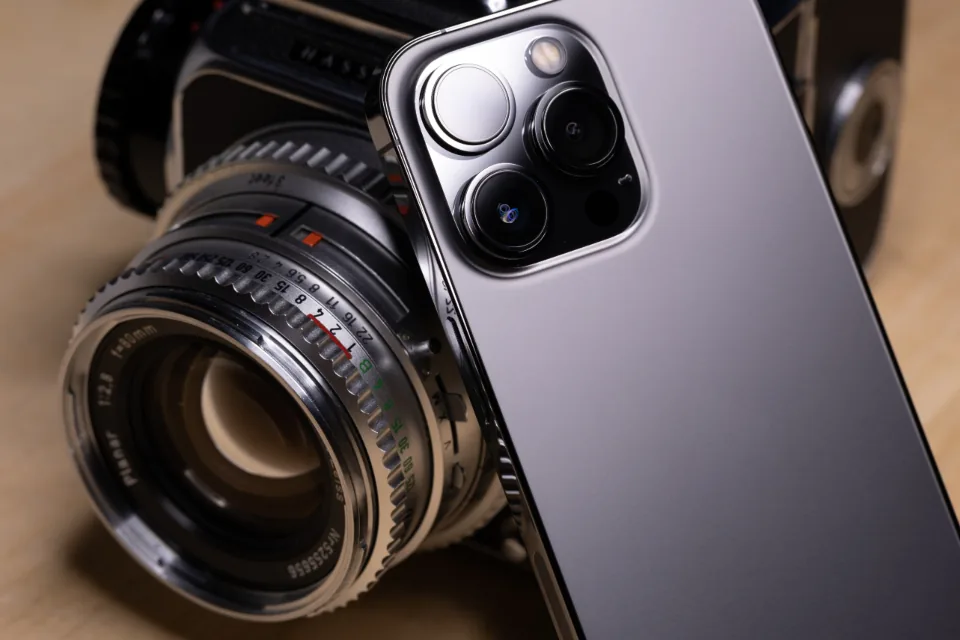 Smartphone camera lenses beside a classic film camera lens