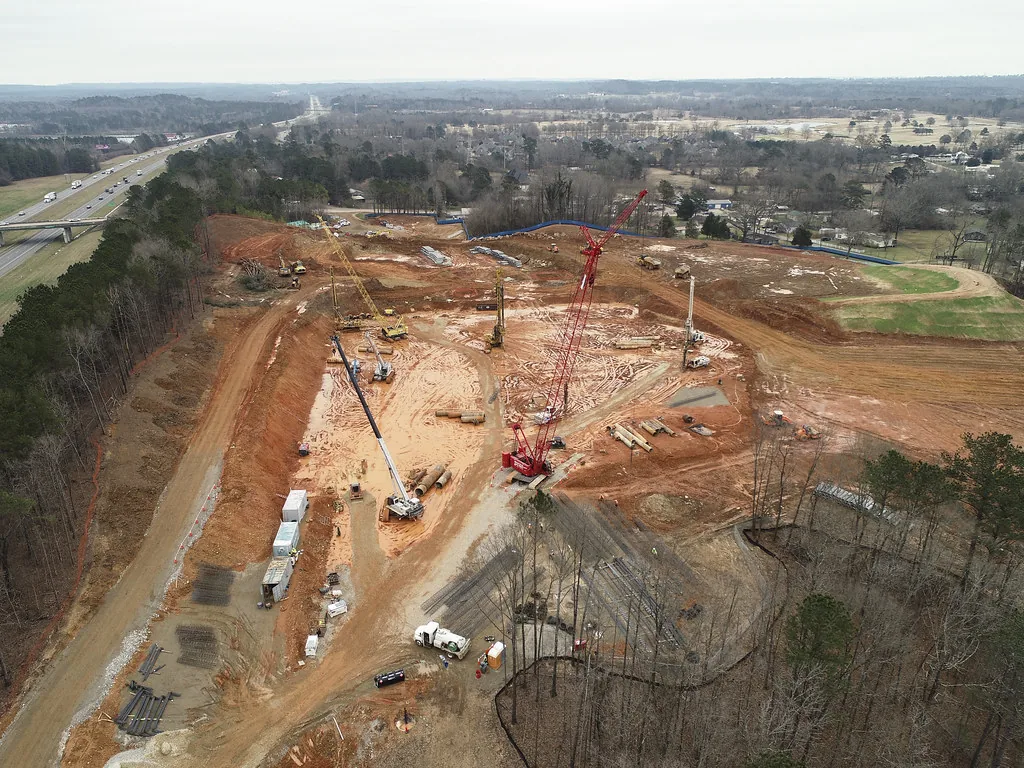 Aerial view of a large graded red-earth construction site with cranes
