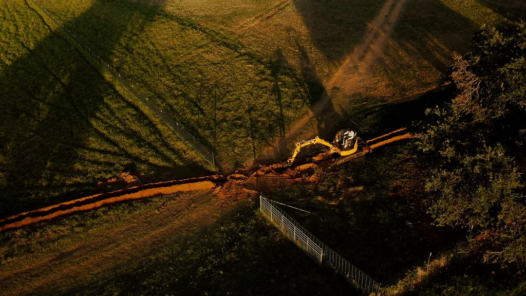 Aerial view of an excavator cutting a trench across a field at sunset